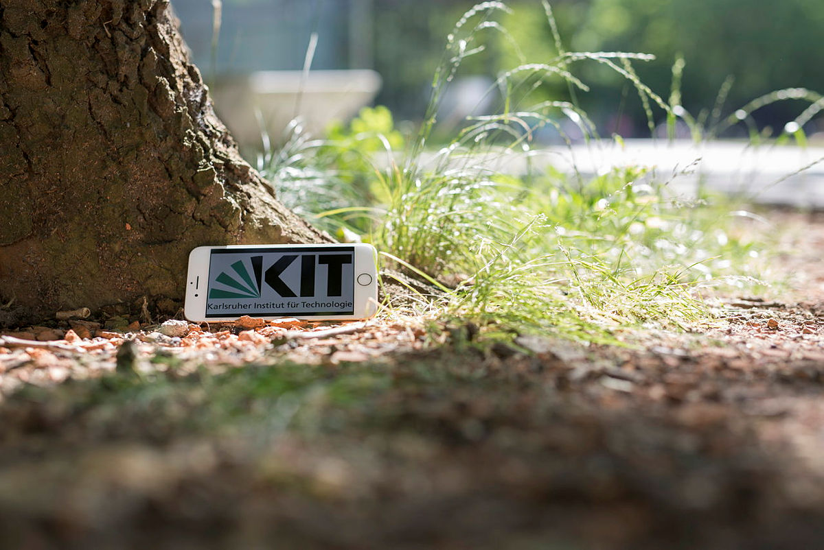 Smartphone mit KIT Logo drauf lehnt an einem Baum