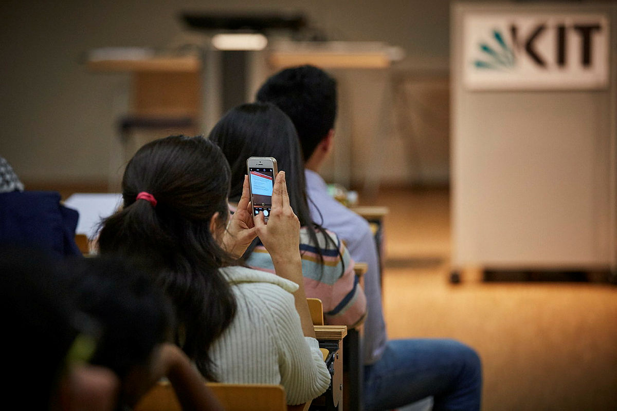 Person fotografiert Folien mit Smartphone in einem Vorlesungssaal am KIT.