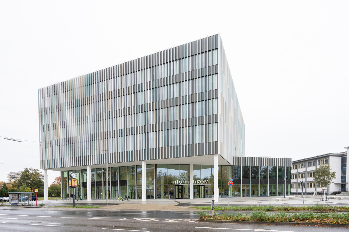 Modernes Bürogebäude mit Glasfront, zweigeschossigem Erdgeschoss und Infomatik/Eingang.