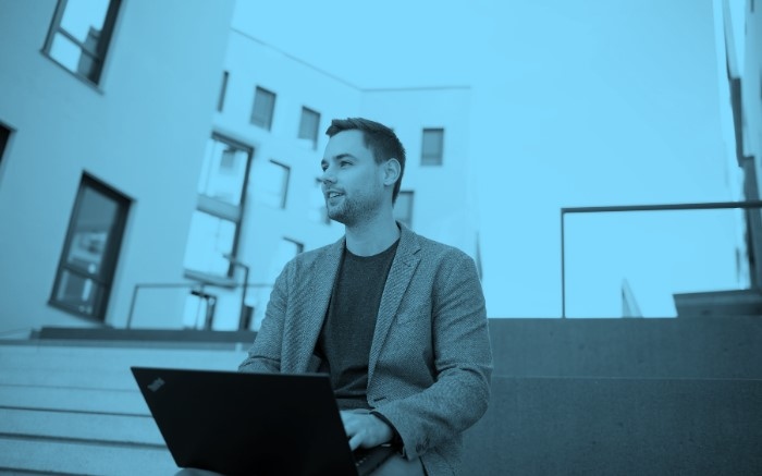 Mann mit Laptop sitzt auf Mauer