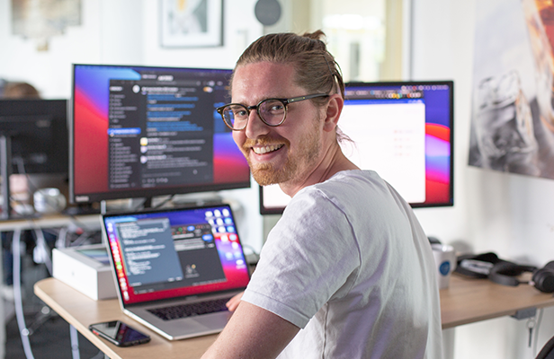 Mann sitzt vor Computer und lächelt in die Kamera